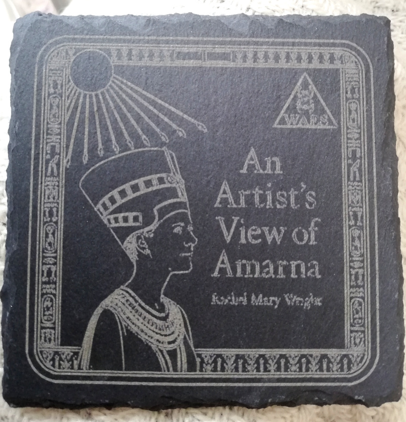 A slate coaster, printed with an image of Nefertiti with the Aten above, arms stretched out in blessing, and beside it the symbol "WAES" in a triangle, and then "An Artist's View of Amarna - Rachel Mary Wright"